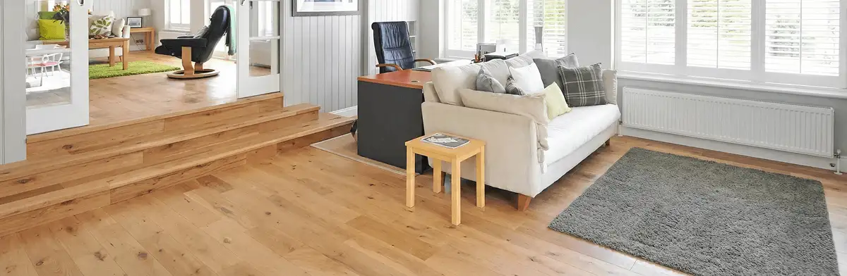 A modern living room with professionally installed laminate flooring, a beige sofa, a small side table, a gray rug, and large windows with white shutters in Springfield, MO